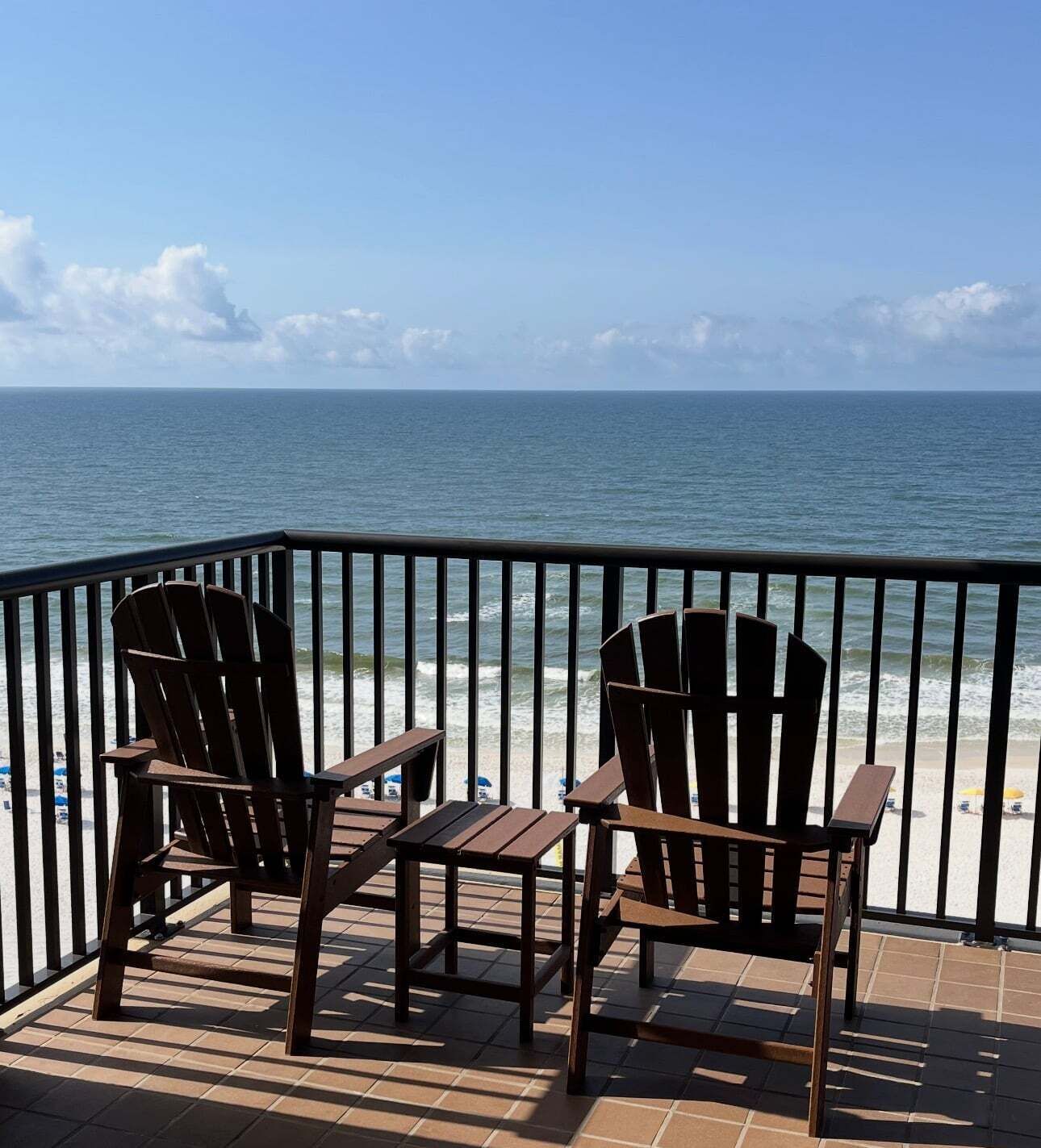 A deck with two Adirondack chairs and a small table, overlooking a beach and the ocean.