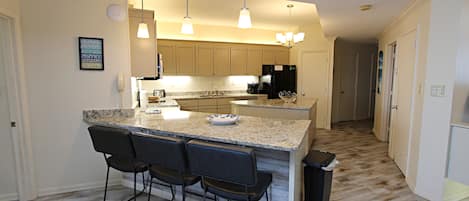 Una cocina moderna con encimera de granito, taburetes de bar e iluminación colgante.