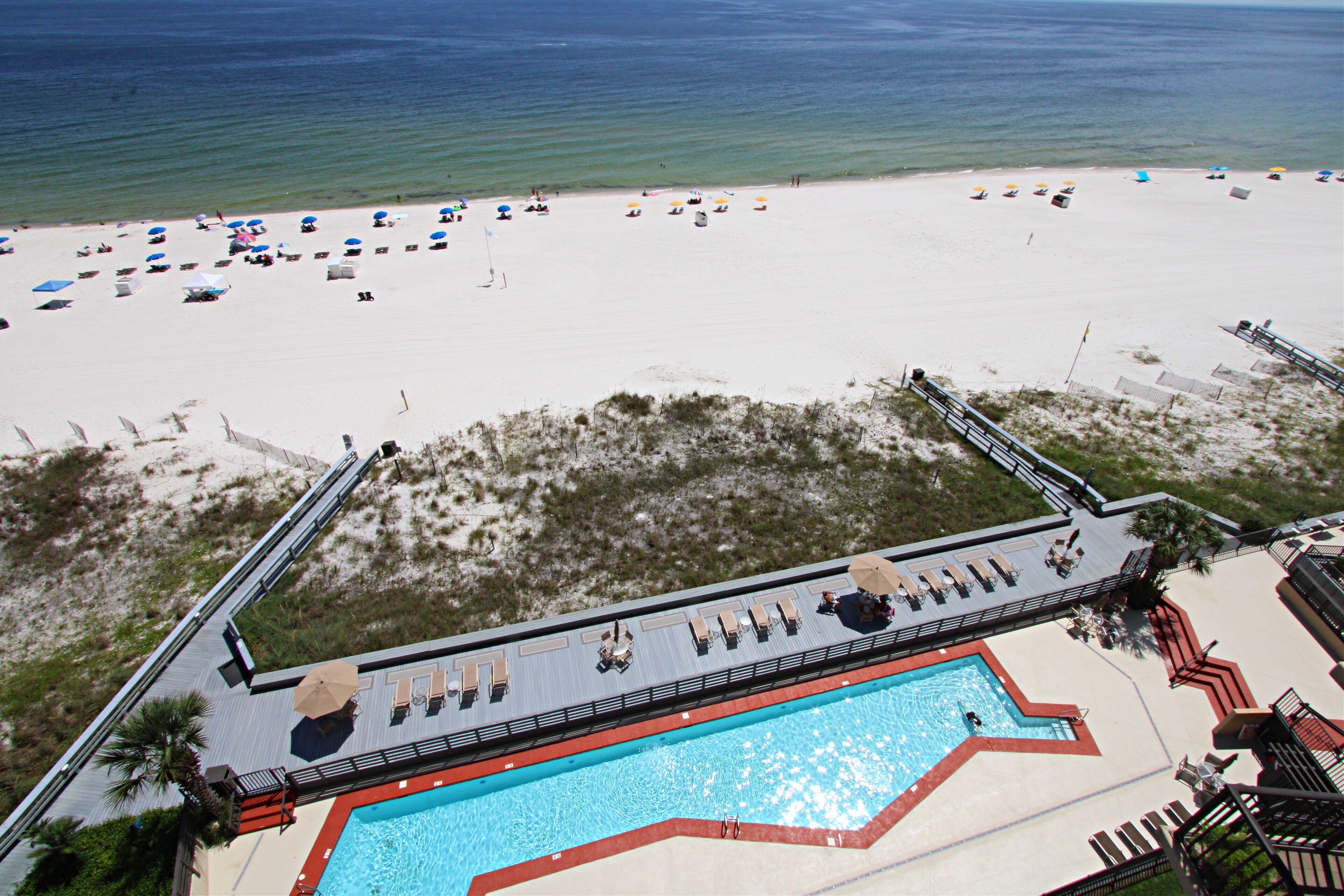 Ett semesterhotell vid stranden med en swimmingpool, parasoller och solstolar.