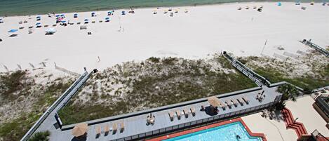 A beach resort with a swimming pool, beach umbrellas, and lounge chairs.