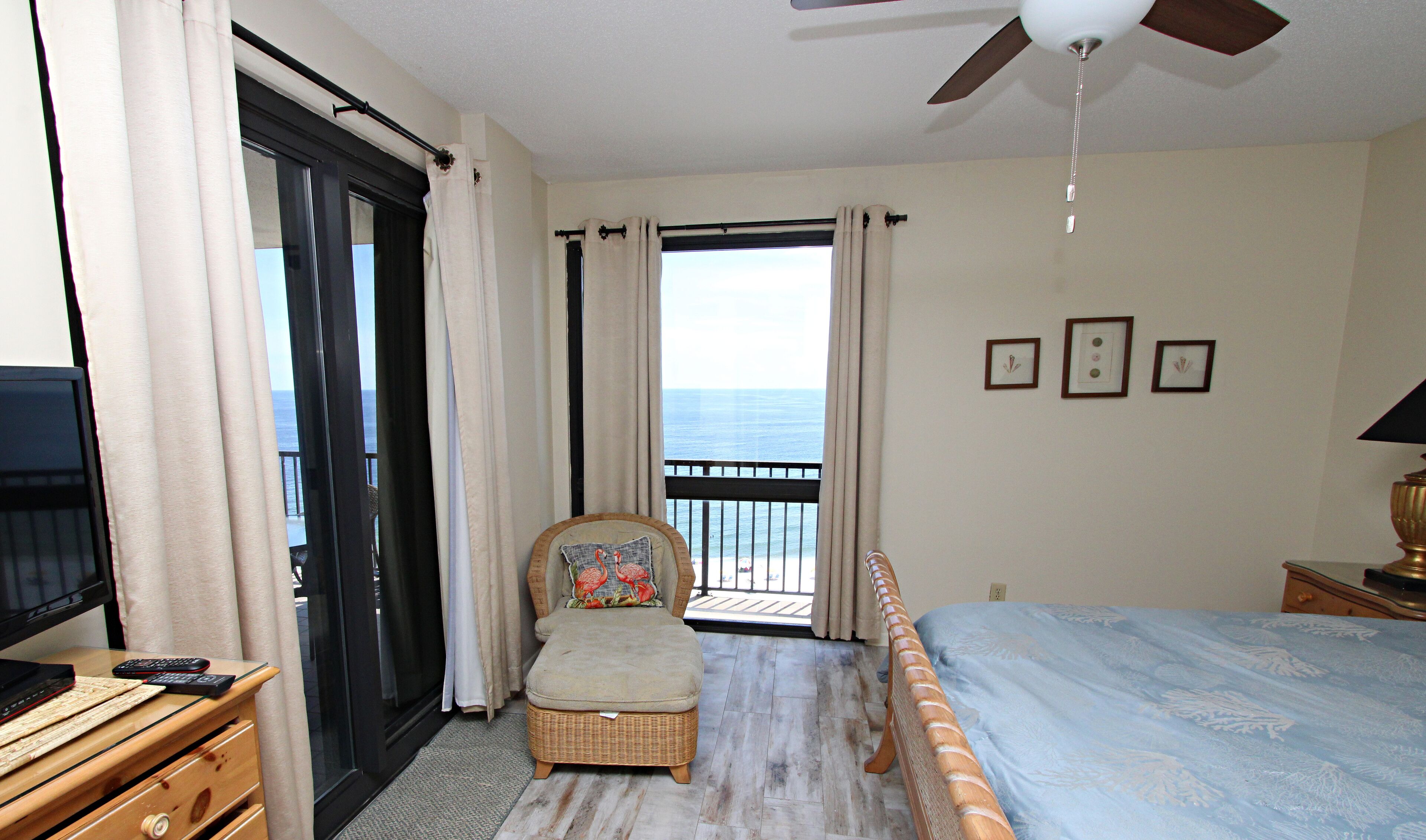 A hotel room with a bed, a chair, a television, and a balcony with a view of the ocean.
