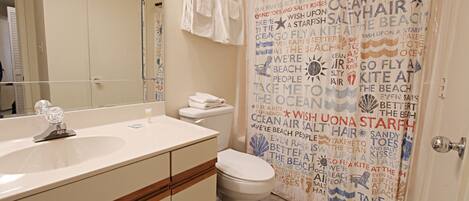 A bathroom with a white sink, mirror, and toilet. There is a shower curtain with text and a towel rack with towels.