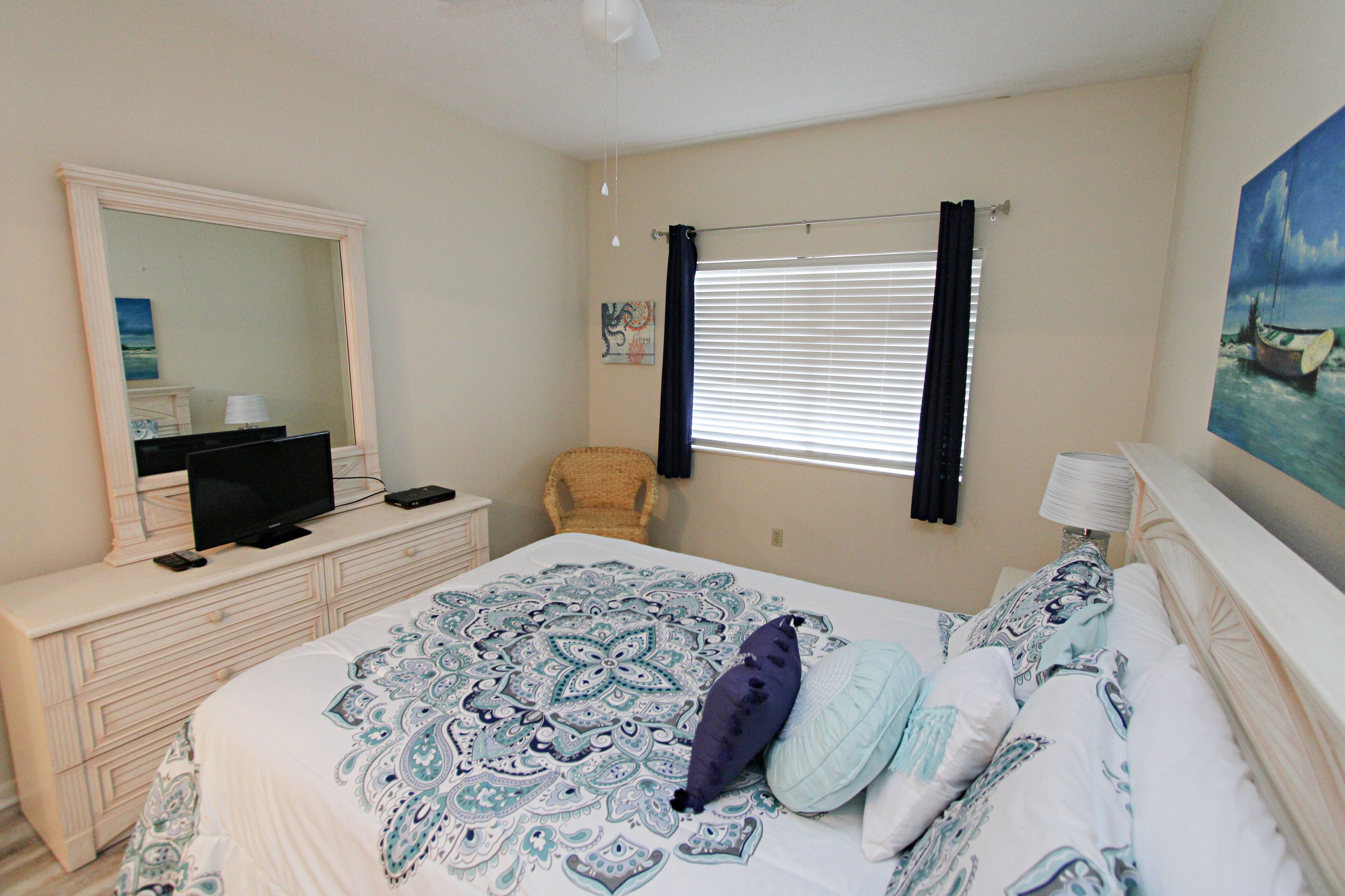 A bedroom with a large bed, a dresser, a television, and a painting on the wall.