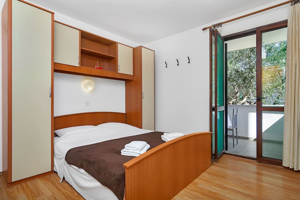 A bedroom with a bed, wooden wardrobe, and a balcony with a chair.