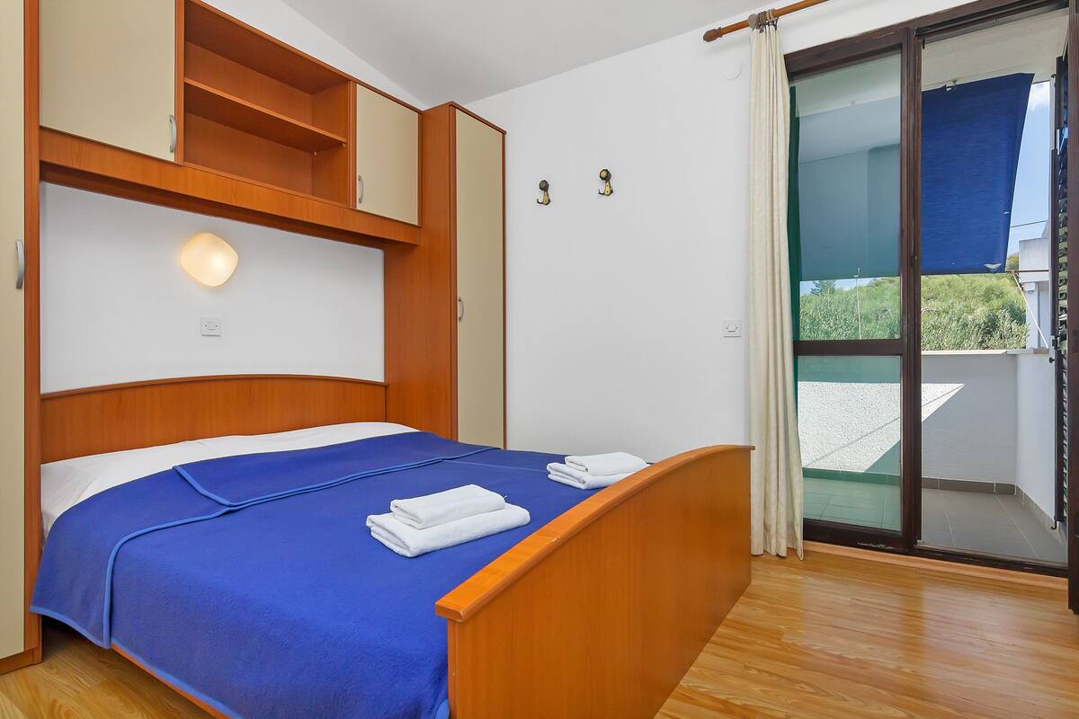 A bedroom with a wooden bed, a blue bedspread, and a view of a balcony through a glass door.