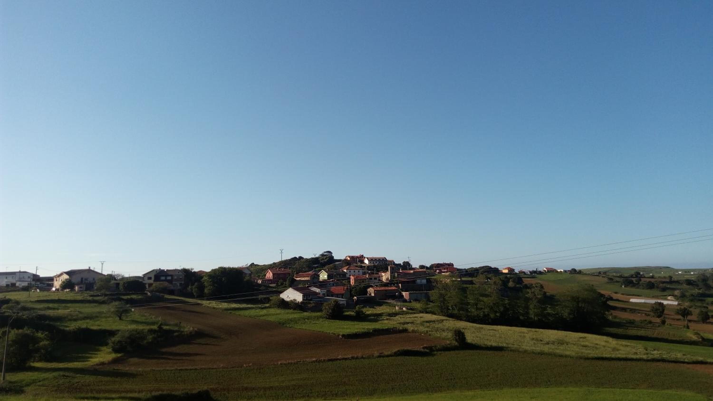 Un poble rural amb cases agrupades en una vessant, envoltat de camps i vegetació.