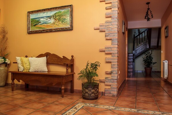 A hallway with a wooden bench, a potted plant, a painting, and a staircase. - Posada Mediavia (Santillana del Mar)