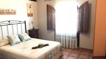A bedroom with a bed, a nightstand, a lamp, a window with curtains, and artwork on the wall.