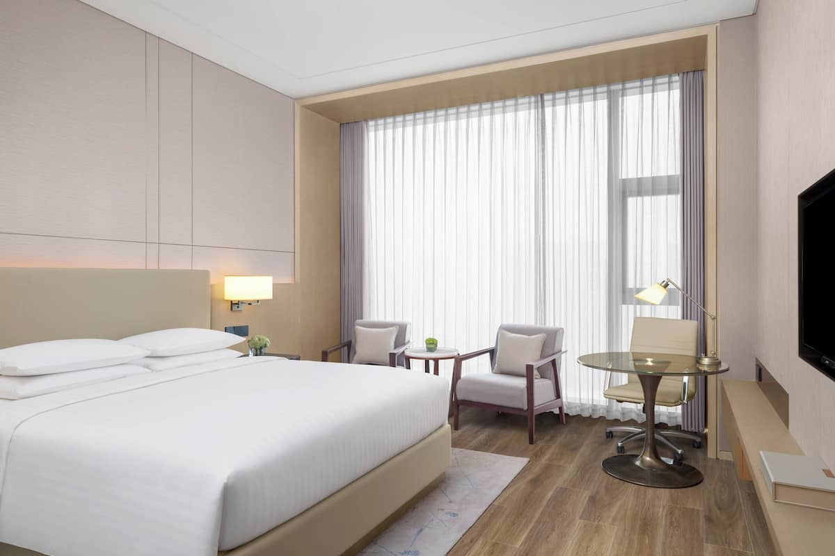 A hotel room with a large bed, a desk with a chair, a TV, and a window with curtains.