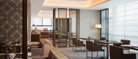 A modern hotel lobby with a dining area, seating arrangements, and a view through a patterned partition.
