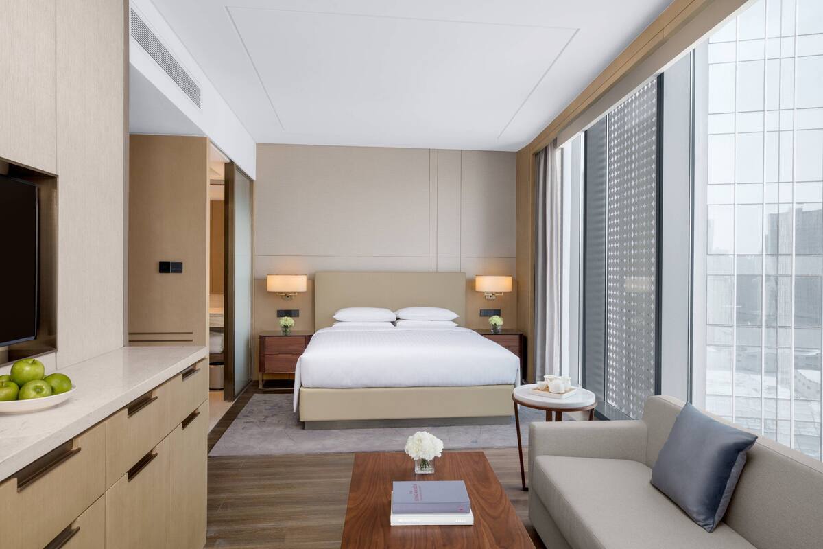 A hotel room with a bed, bedside tables, a coffee table, a sofa, and a large window with a city view.
