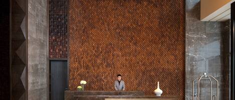 Un comptoir d’accueil au design moderne, un mur orné de motifs et un sol en marbre.