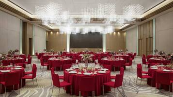 Un amplio salón de banquetes con mesas redondas dispuestas para comer, un escenario central y una lámpara de araña moderna.