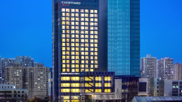 Un hotel Courtyard Marriott amb una façana moderna de vidre, envoltat d'altres edificis.
