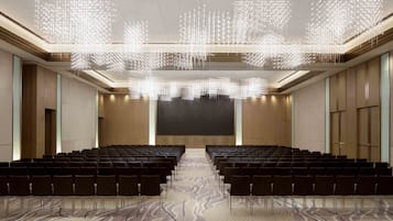 A conference room with rows of chairs, a large screen, and a ceiling light fixture.