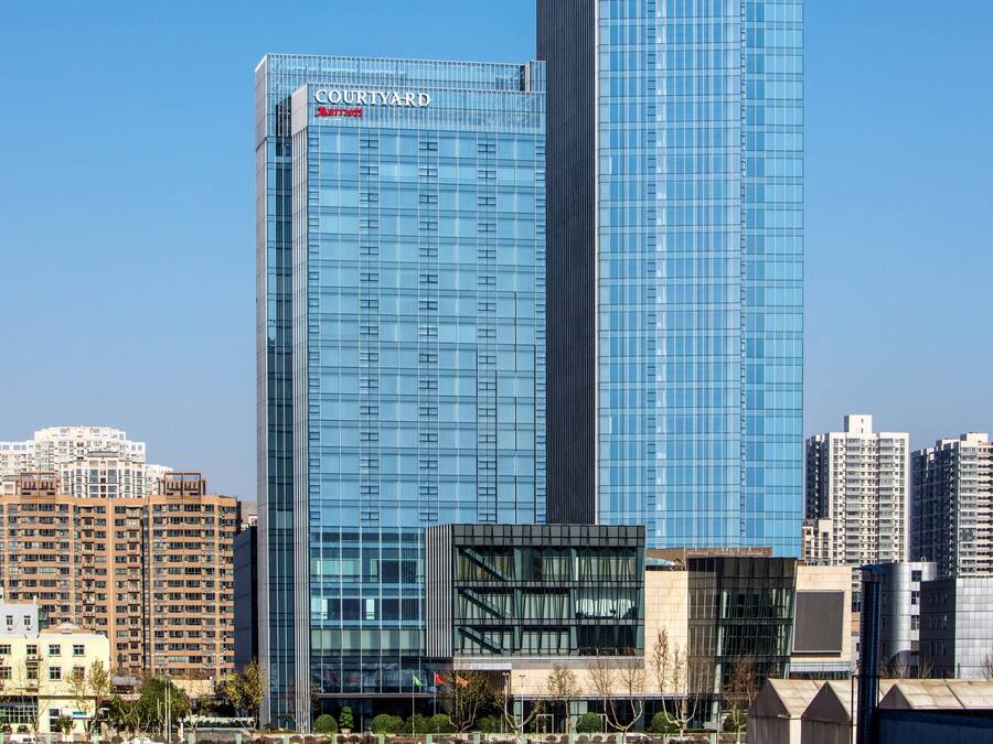 A modern high-rise hotel with a Courtyard by Marriott sign, surrounded by other buildings.
