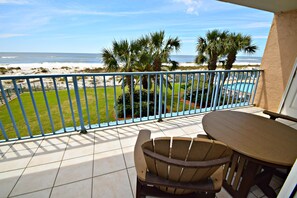 A balcony with a view of the beach, a pool, and palm trees.