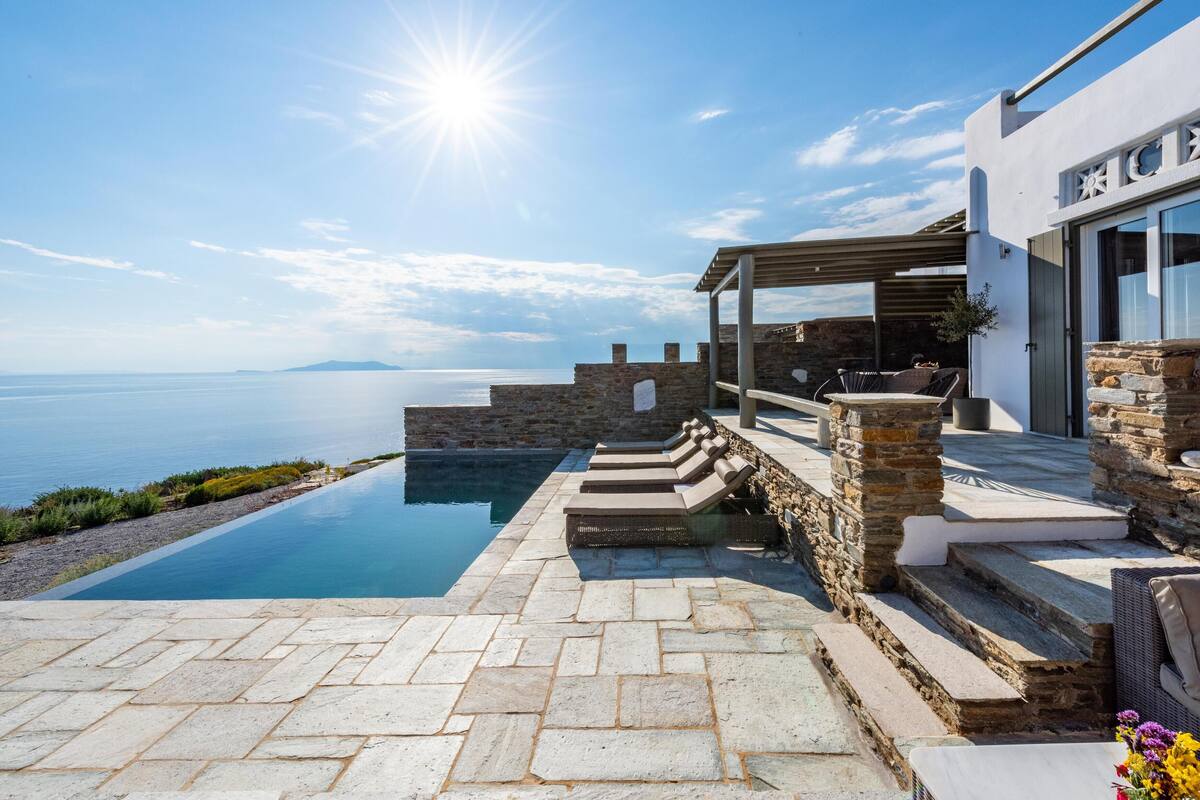A modern outdoor pool area with stone steps leading to a covered seating area, overlooking a body of water.