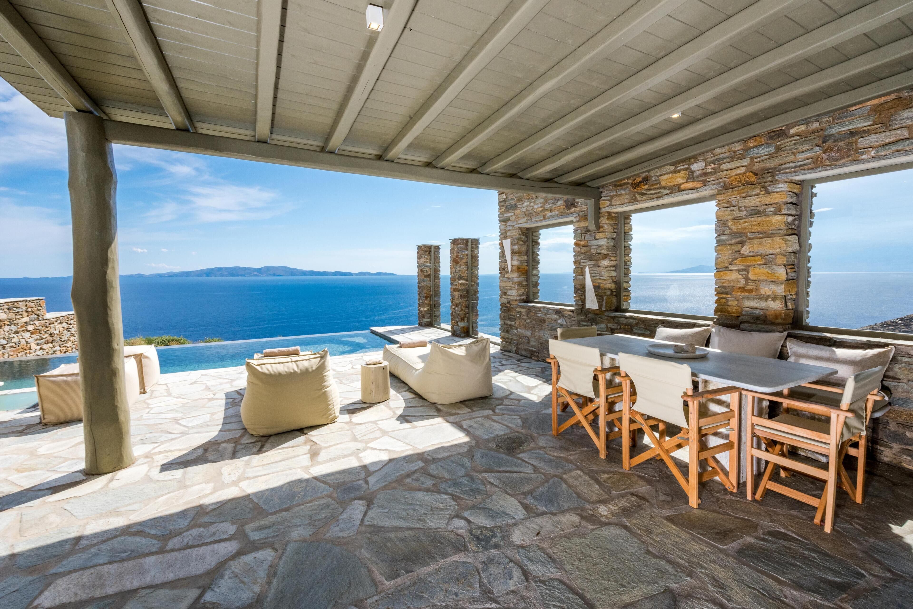 An outdoor seating area with stone flooring, a pool, and a view of the sea.