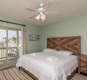 Um quarto limpo e bem iluminado com cama, ventilador de teto, vista para o exterior e varanda.