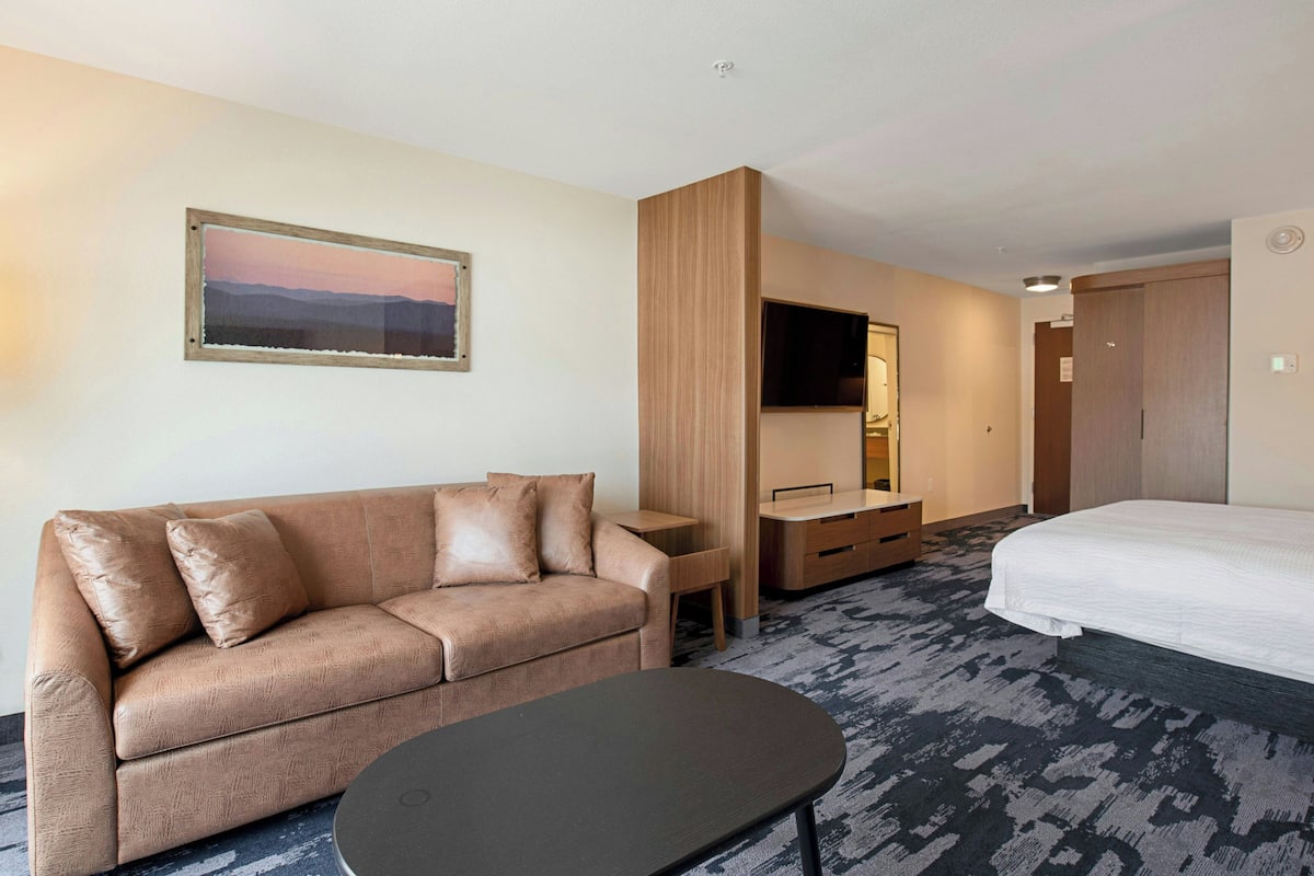 A hotel room with a sofa, a small table, a bed, a TV, and a wooden cabinet.