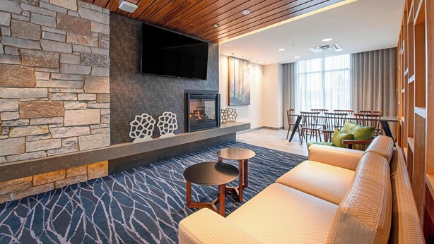 A modern hotel lobby with a stone wall, a flat-screen TV, a fireplace, a sofa, and a dining area. - Fairfield Inn & Suites by Marriott Duluth Waterfront (Duluth)
