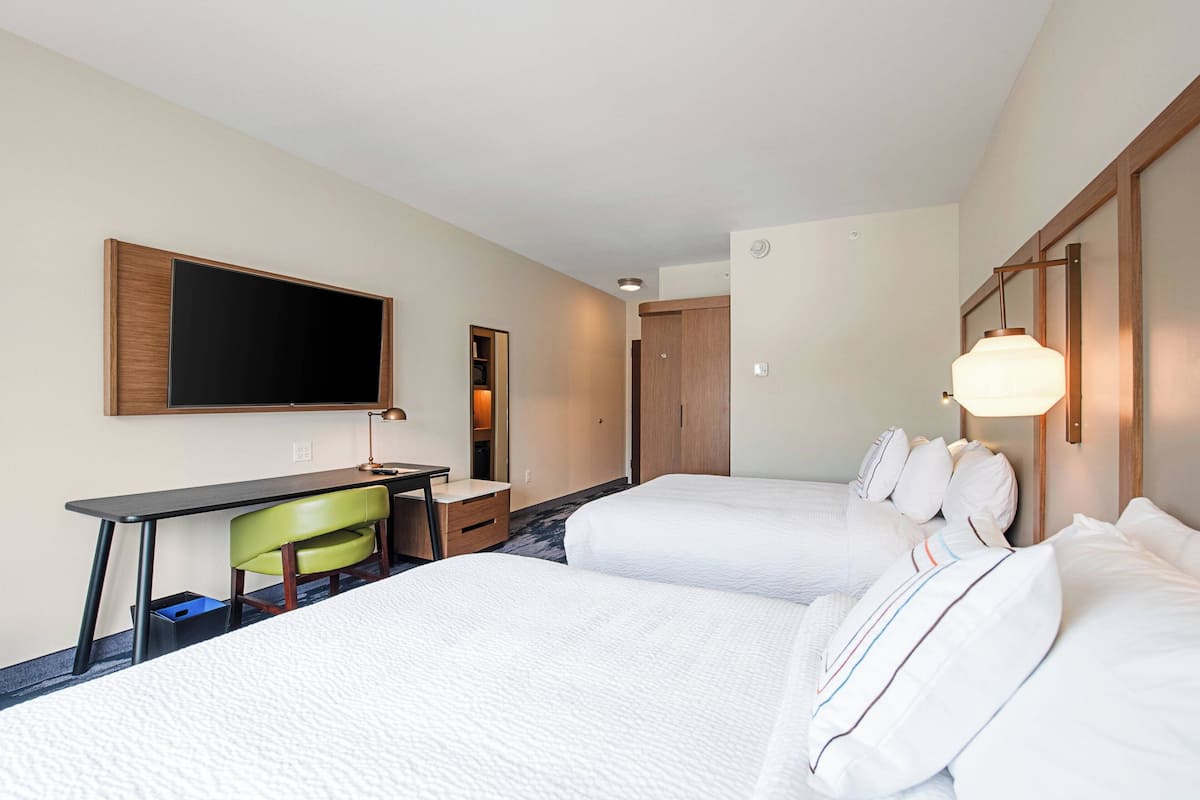 A hotel room with two beds, a desk, a chair, a television, and a lamp.
