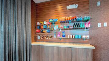 A hotel reception area with a wooden counter, shelves stocked with toiletries, and a patterned wall.