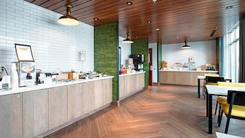 Interior moderno de restaurante com soalho de madeira, balcão com diversos alimentos e área de estar com cadeiras amarelas.