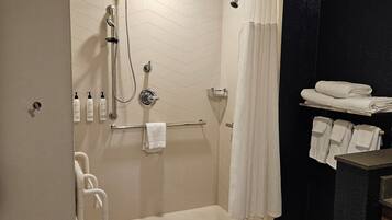A modern bathroom with a walk-in shower, a handrail, a towel rack, and a small sink area.