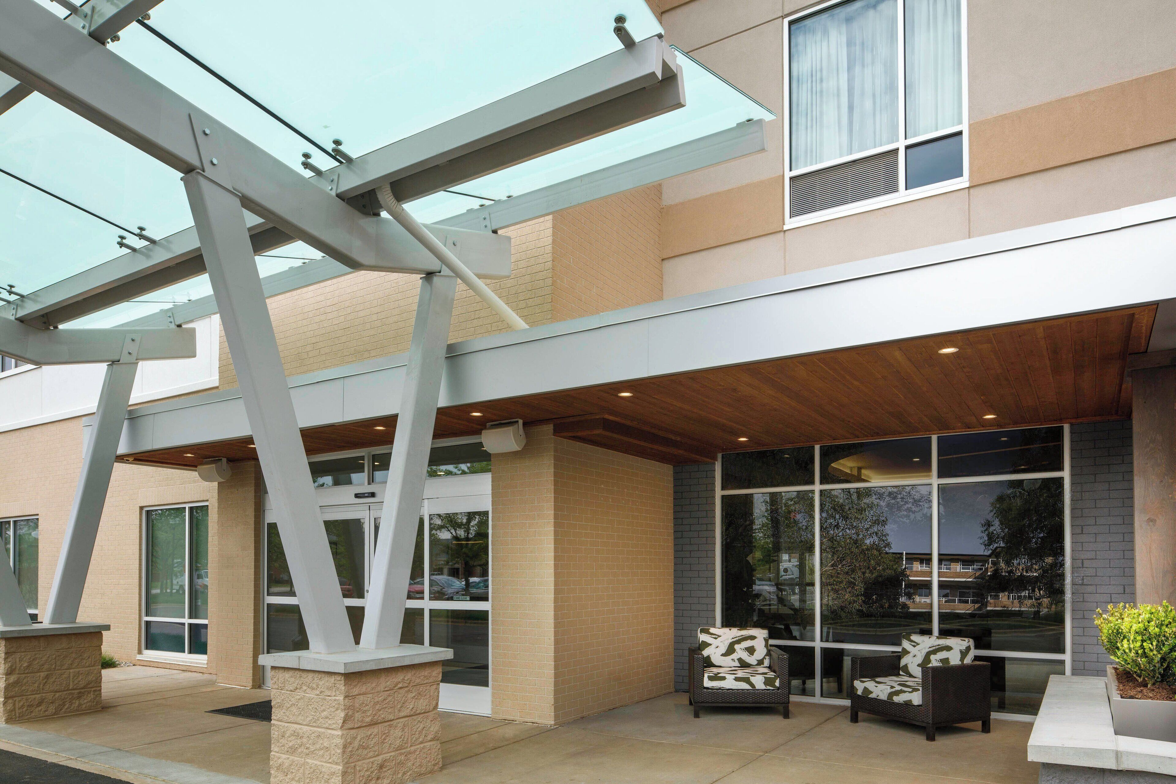 A modern building with a glass entrance, outdoor seating area, and a covered patio.
