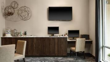 A modern reception area with a wooden desk, two monitors, and a large TV. There are decorative spherical objects on the wall and a window with a view of the outside.