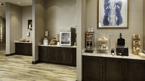 A hotel lobby with a reception desk, a coffee machine, a refrigerator, and a framed artwork on the wall.