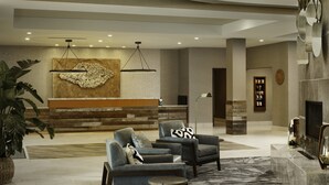 A modern lobby with a reception desk, two armchairs, a large abstract wall art, a potted plant, and a fireplace.