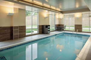 Piscina con agua azul cristalina, rodeada por un solárium con azulejos y una zona de estar con sillas y una mesa.