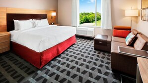 A hotel room with a large bed, a sofa, a desk, and a window with a view of greenery.