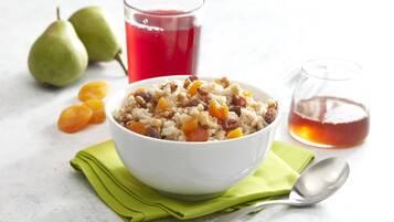 Un bol de porridge agrémenté de fruits et de noix, un verre de jus rouge et des poires sur une surface blanche.
