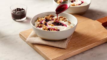 A bowl of yogurt with granola and berries on a wooden board.