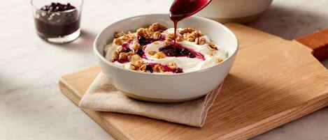 Un tazón de yogur con granola y frutos rojos sobre una tabla de madera.