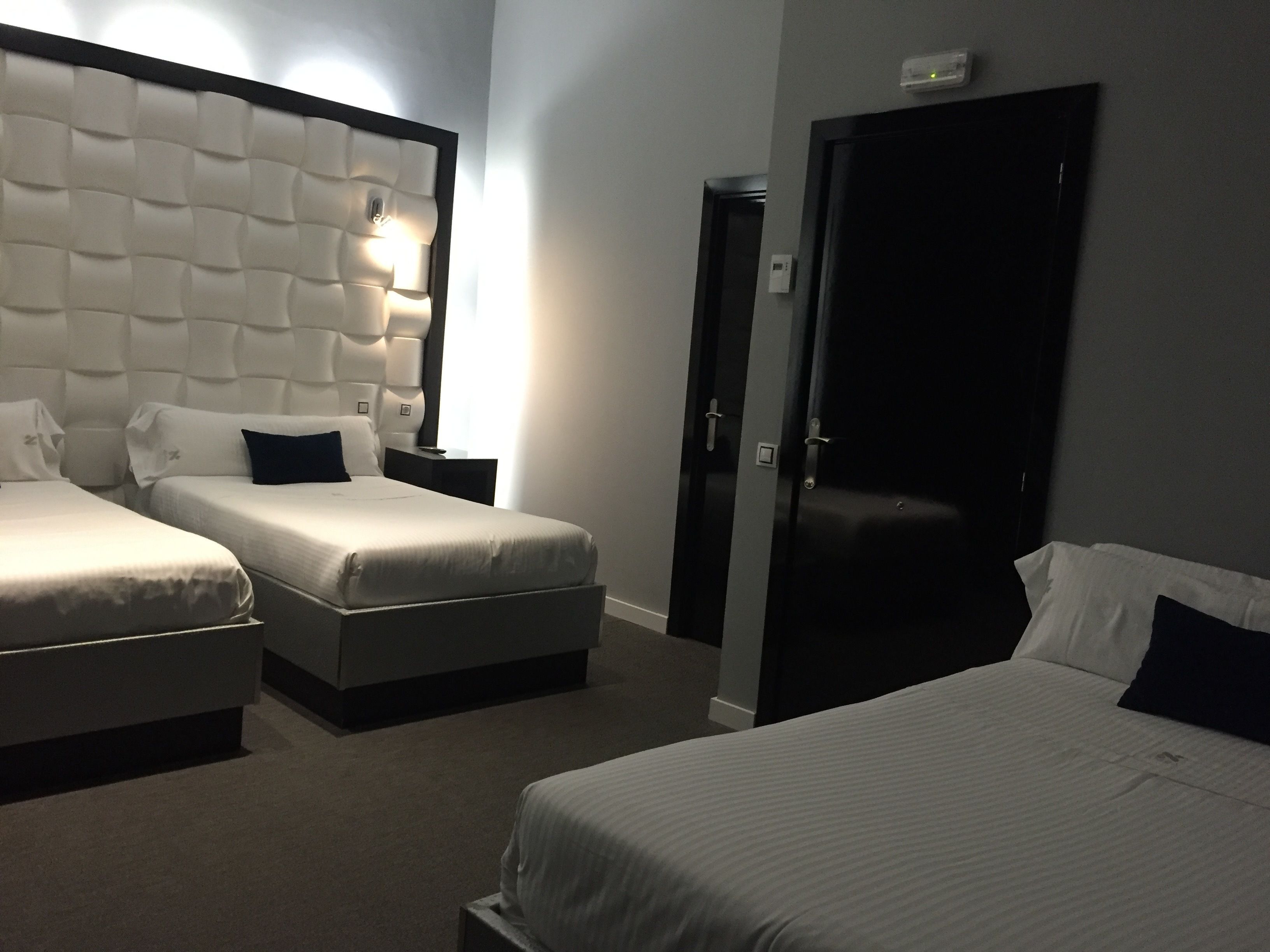 Habitación de hotel con dos camas, un cabecero grande y acolchado, una mesita de noche y una puerta.