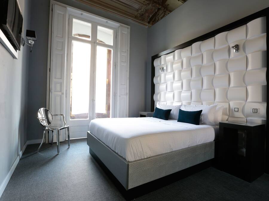 Un dormitorio moderno con una cama grande, una silla y un cabecero original.