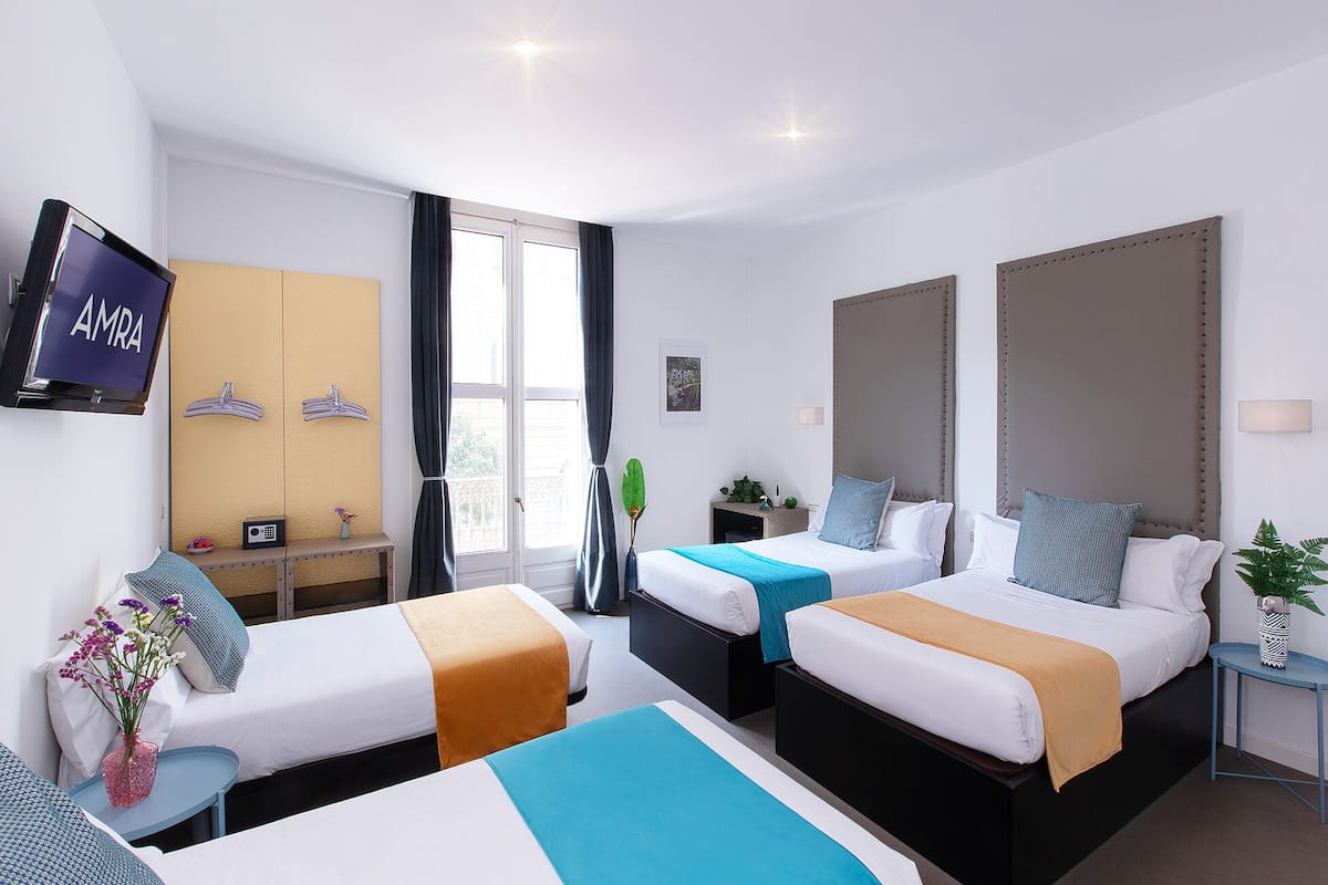 A hotel room with two beds, a TV, a desk, and a window with curtains.