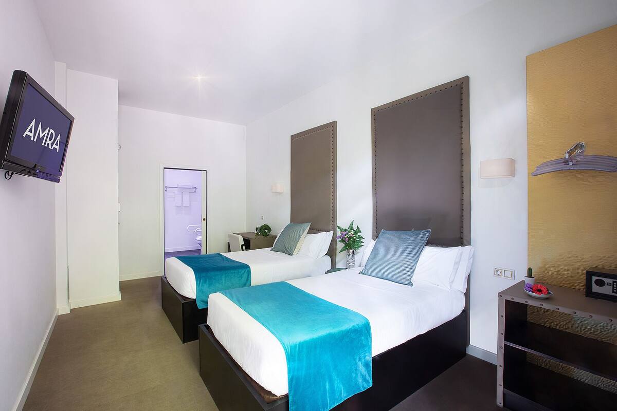 A hotel room with two beds, a desk, a TV, and a bathroom visible through an open door.