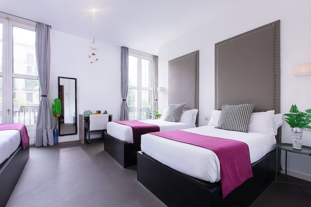 A hotel room with two beds, a desk, a chair, a mirror, and a window with curtains.