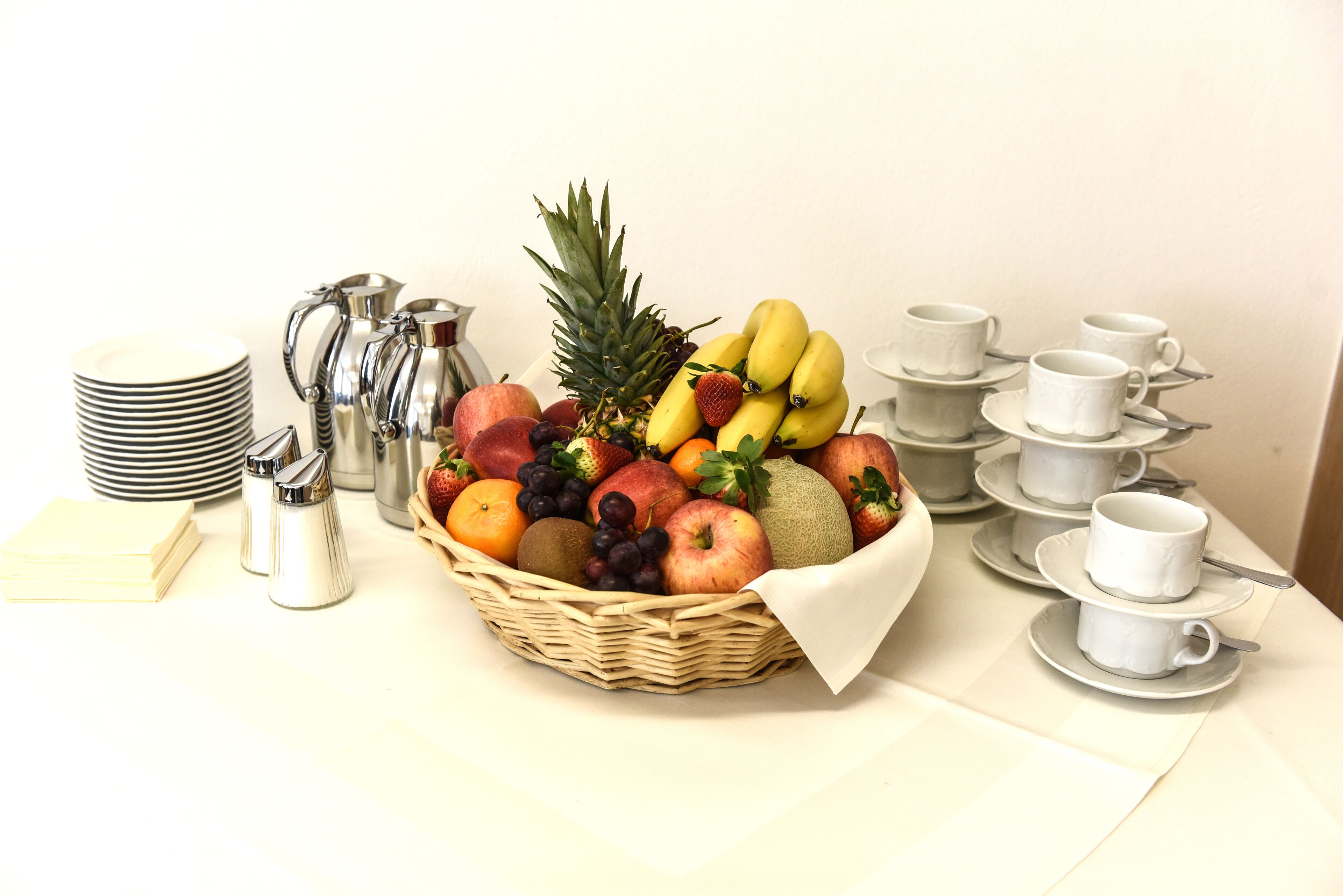 A fruit basket with a variety of fruits and a coffee pot on a table.