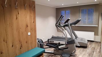 A gym with a treadmill, a bench, and a wooden wall with hooks.