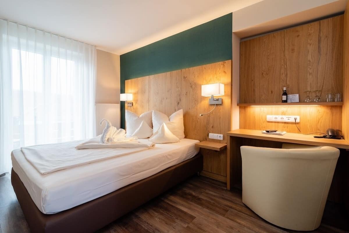 A hotel room with a large bed, a desk with a chair, and a wooden headboard.