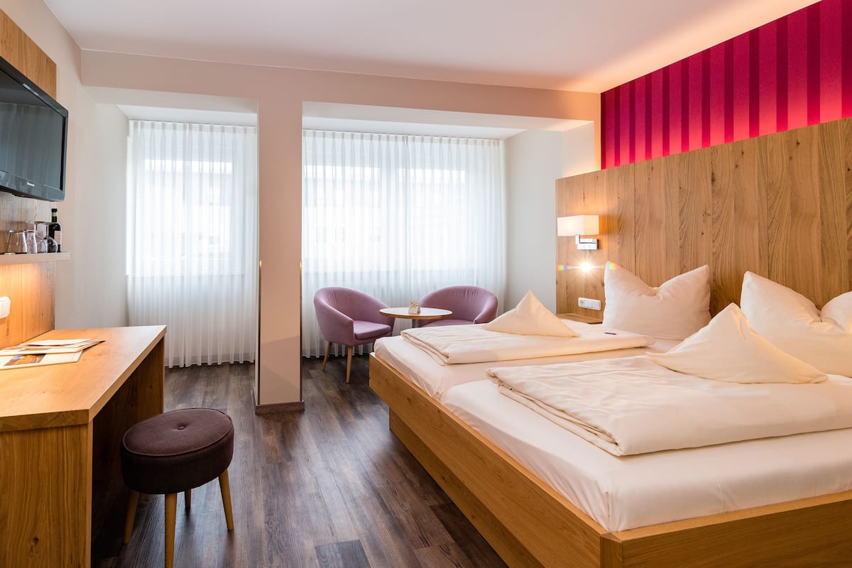 A hotel room with a wooden bed, a desk, a chair, and a small table.