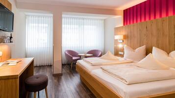 Quarto de hotel com cama de madeira, escrivaninha, cadeira e uma pequena mesa.