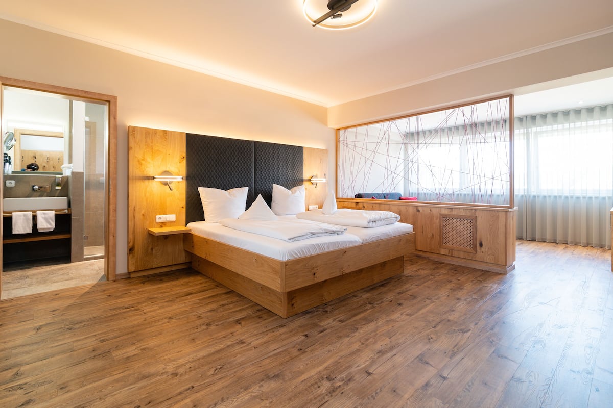 A modern bedroom with a wooden bed, built-in headboard, bedside tables, and a large window with a view.